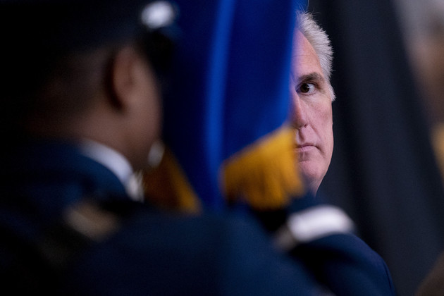 House Minority Leader Kevin McCarthy mostly obscured by a military officer and flag.