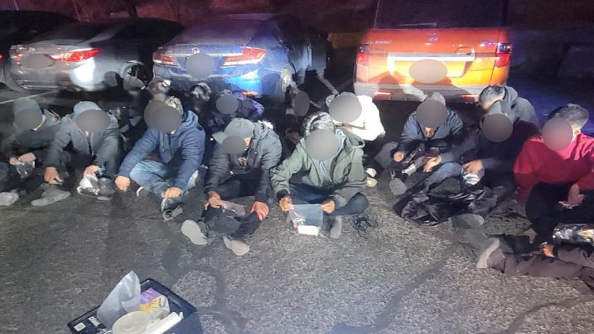 About a dozen detained migrants sit on the concrete