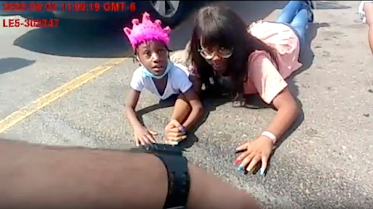 6-year-old Lovely Gilliam looks up at a police officer as she and her family members lie in a parking lot after they were wrongfully forced out of their car on Aug. 2, 2020, in Aurora, Colo.