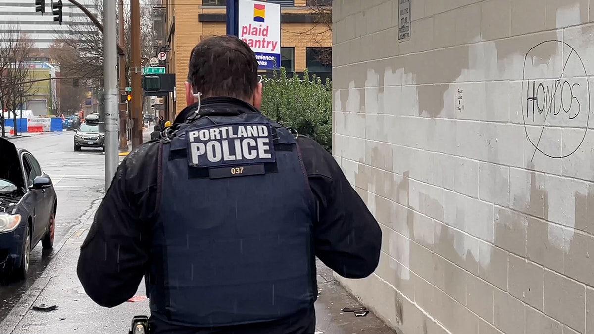 Portland police officer walks by wall with word 