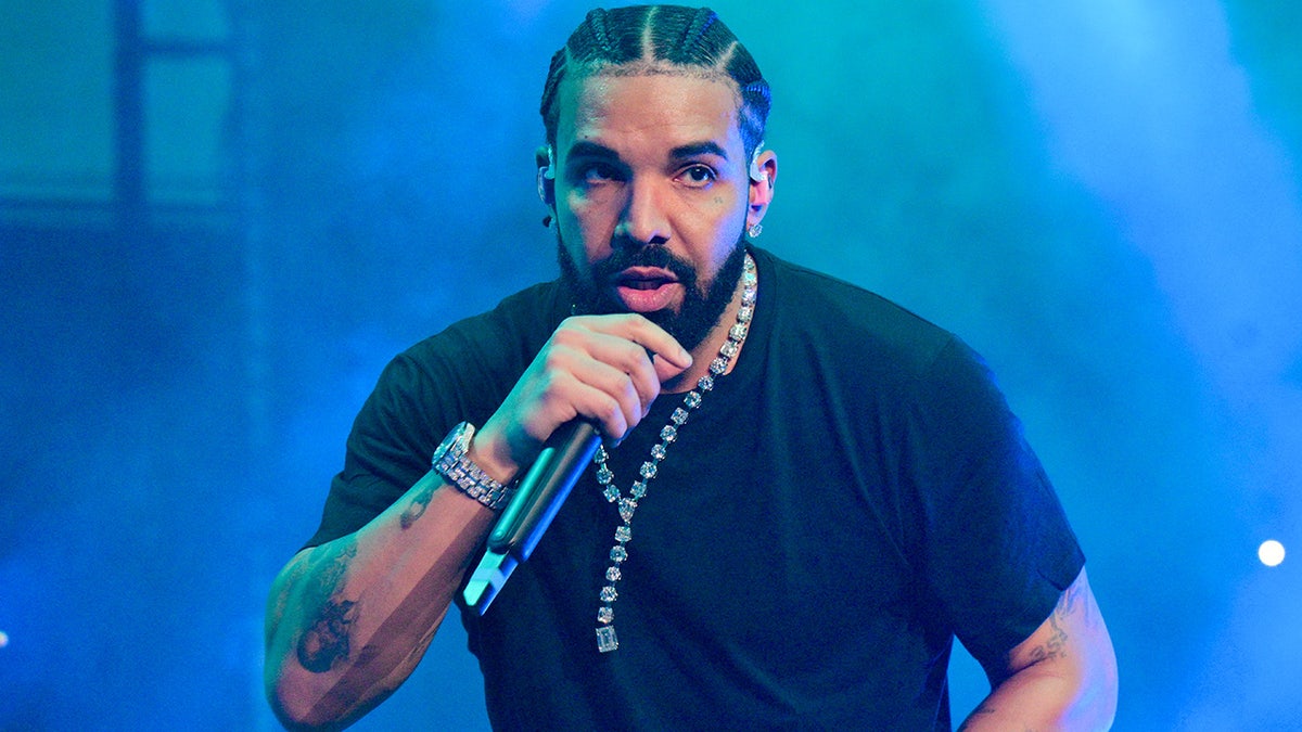 Drake in a black shirt and long chain raps into a microphone while onstage in Atlanta