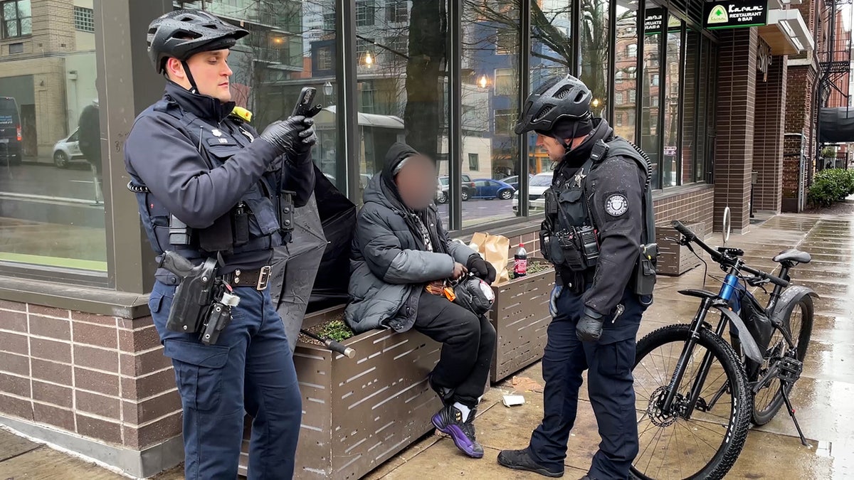 Oregon State Police troopers talk to a woman on the sidewalk in Portland